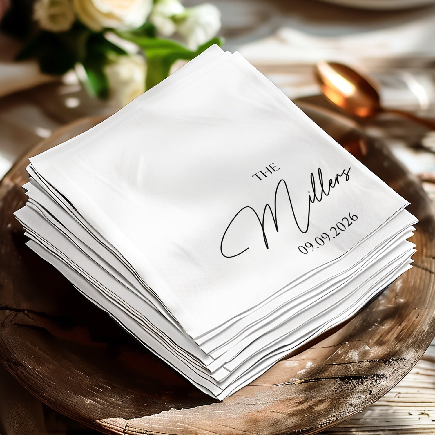 White napkins stacked on a wooden charger, with "The Millers 09.09.2026" printed.